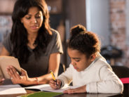A Teacher Who Gave Lots of Homework Reconsiders Mother looking at cute little daughter doing homework at home, homework help concept