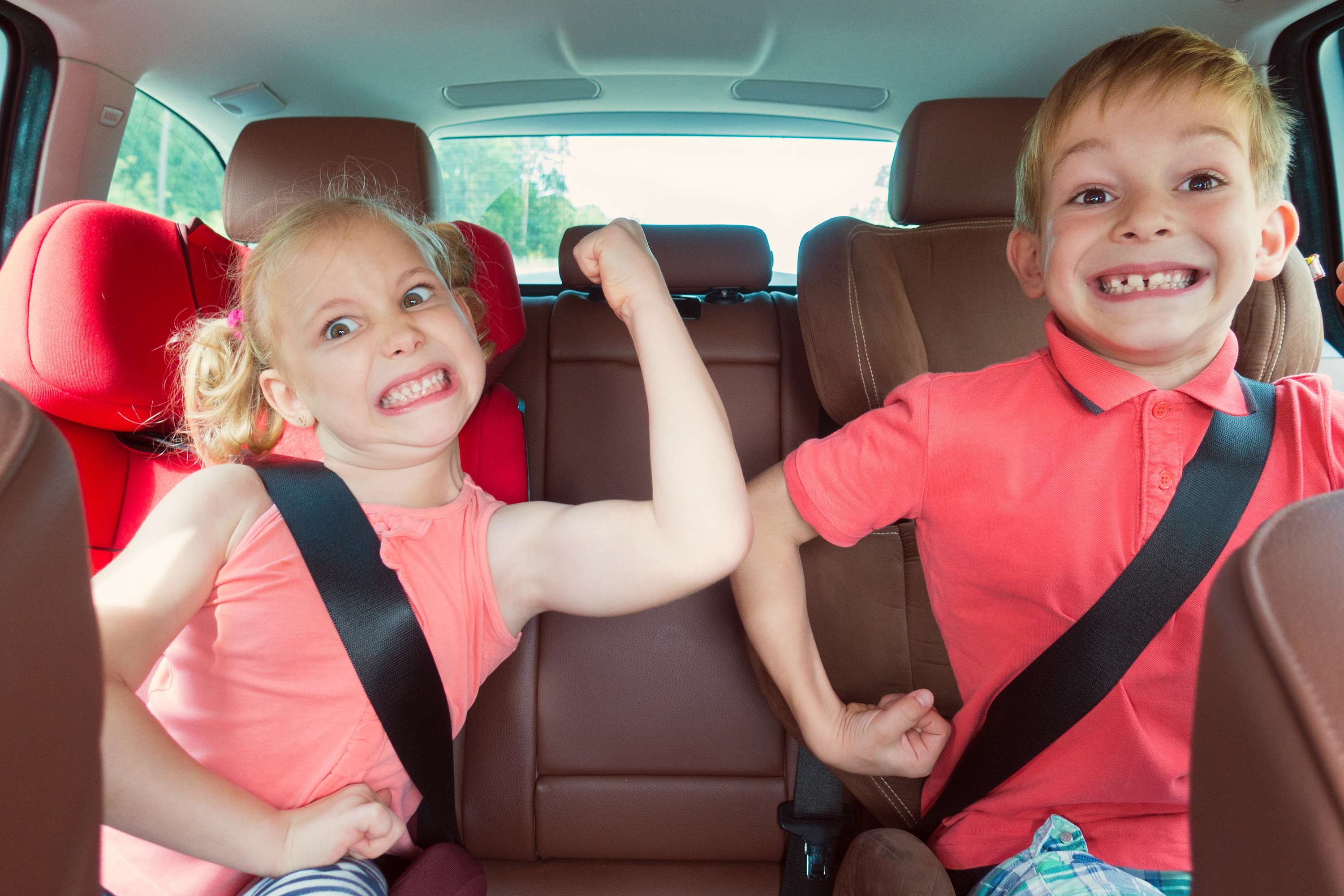 Happy kids, adorable girl with her brother sitting together in modern car locked with safety belts enjoying family vacation trip on summer weekend