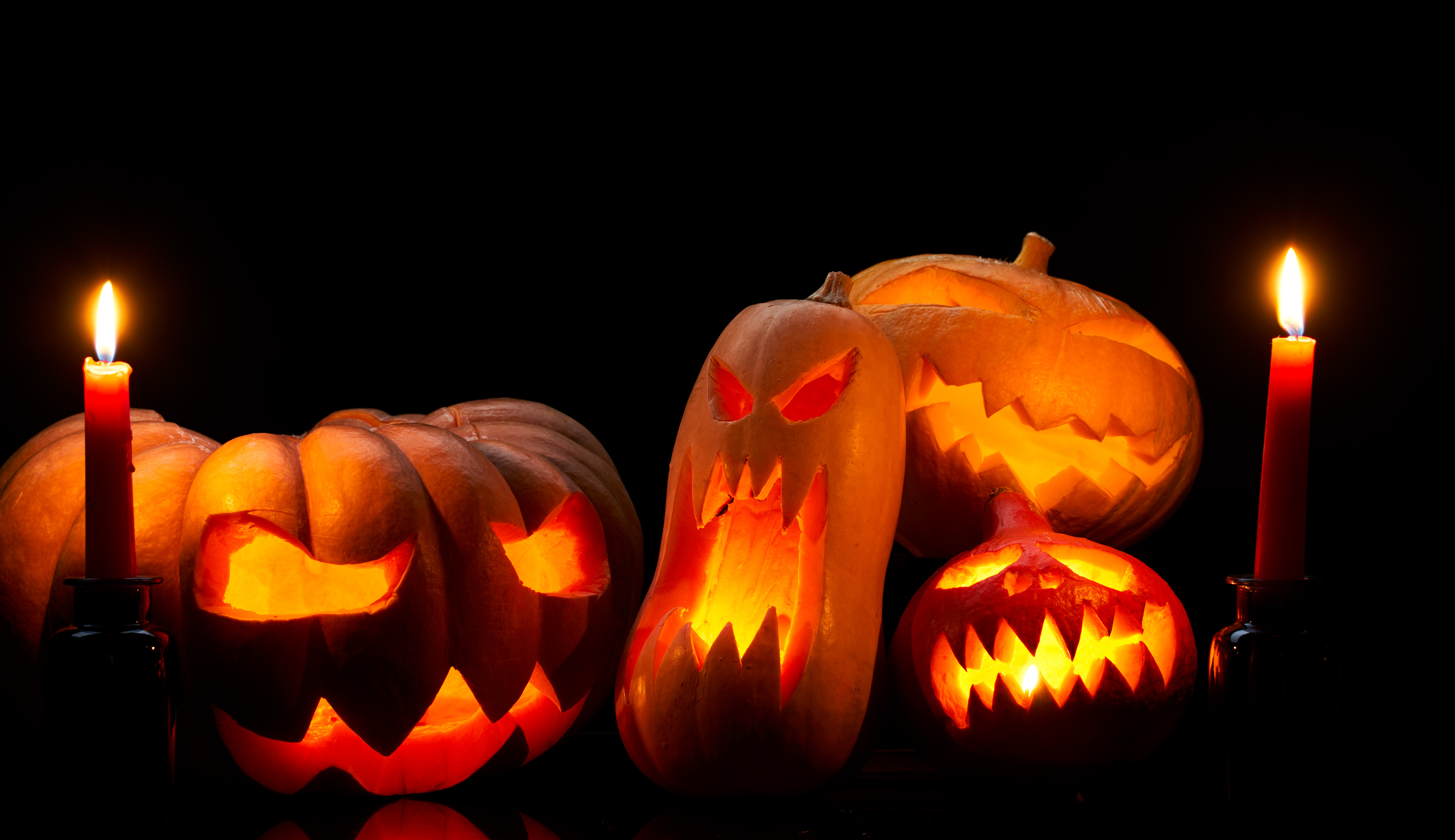 Photo of halloween pumpkins with burning mouths, candles on empty black background in studio