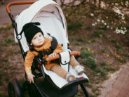 A baby in a beige jacket in a stroller on a walk in the spring Park.