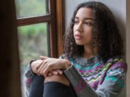 Beautiful mixed race African American girl teenager female young woman sad depressed or thoughtful looking out of a window